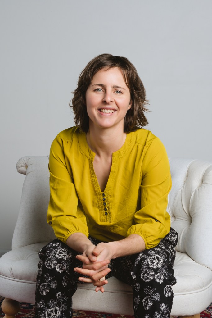 Common Good Resolution Director Phoebe sitting on a chair smiling at camera.